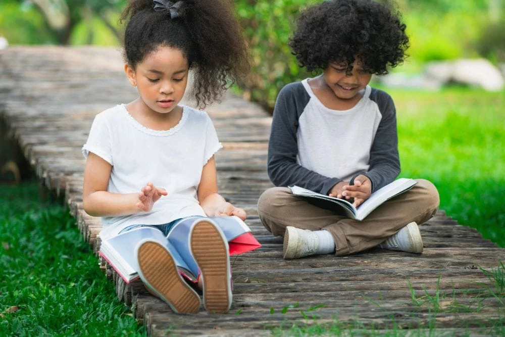 Two young Black kids reading on the ground outside