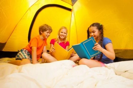 Three preteens reading books inside a tent