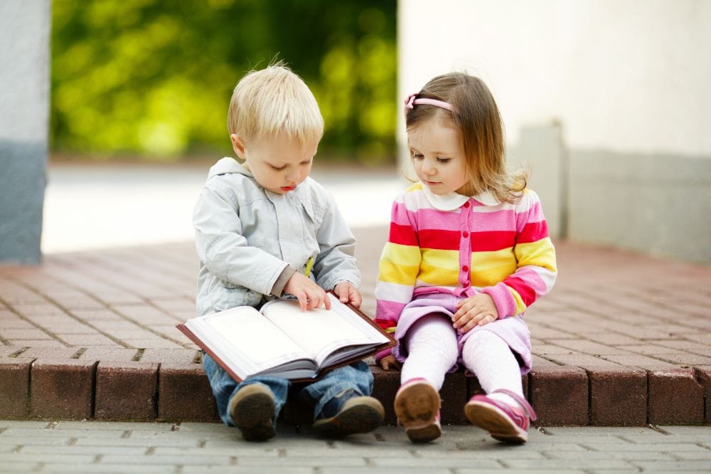 Two cute toddlers reading a book together outdoors