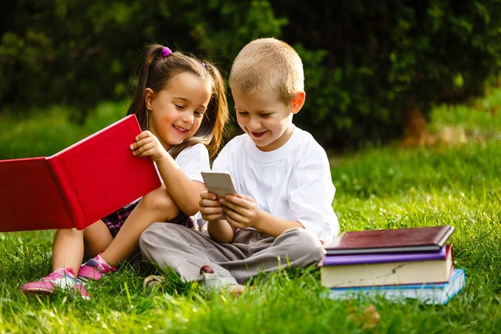 Two adorable preschoolers reading books on the grass