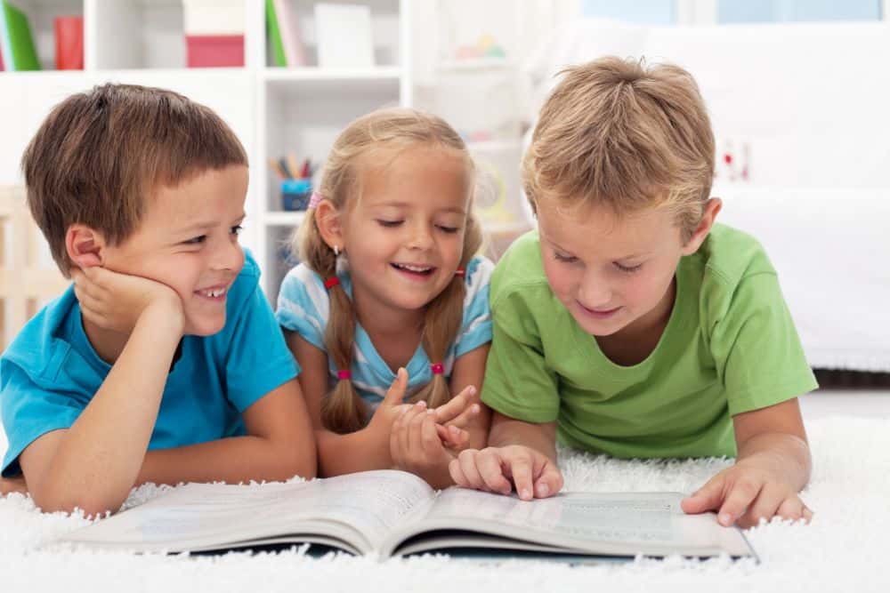 Three cute laughing kids reading a book on the floor