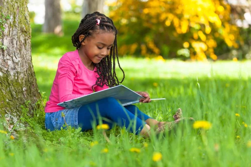 Beautiful Black girl sitting underneath a tree while reading a book