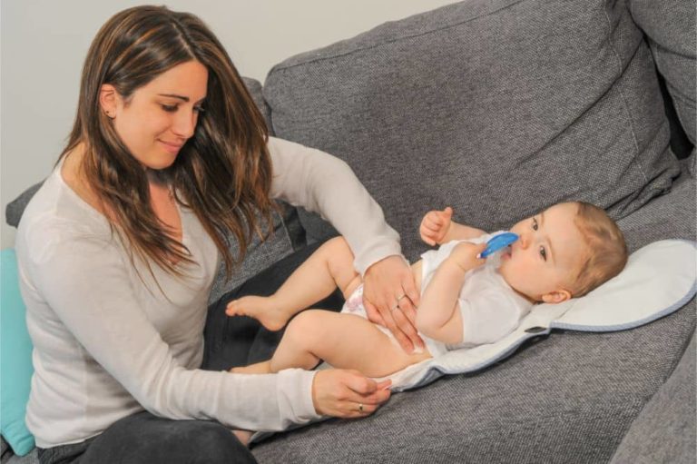 Brunette mom changing her baby's diaper on the sofa
