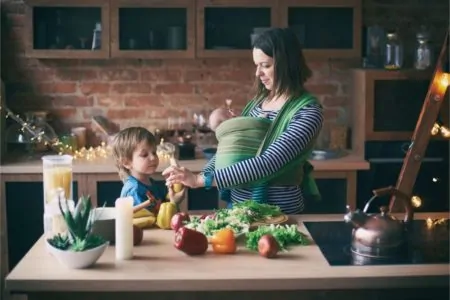 Mother preparing food in the kitchen with baby and young son