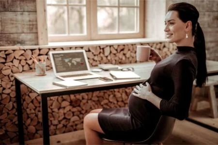 Pregnant woman in black dress sitting down in her office