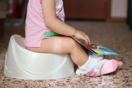 Toddler sitting on a potty seat while reading a book