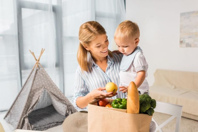 Smiling mother showing the groceries to her baby while carrying him