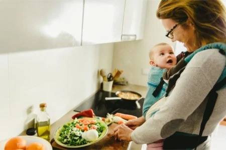 Mother smiling at her baby in carrier while making breakfast