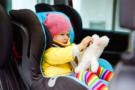Toddler playing with teddy bear in her car seat