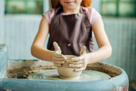 Little girl molding a cup with a pottery wheel