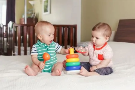 Two cute babies playing with stacking rings on the bed
