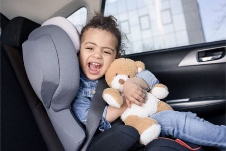 Happy little girl holding her teddy bear in a child car seat