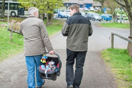 Grandfather carrying his grandson in a car seat while walking with his son