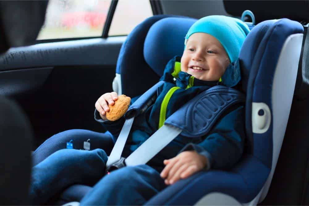 Smiling toddler in a car seat eating a cookie