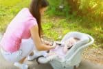 Mom kneeling on the ground while fastening seat belt on her baby's car seat