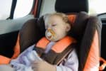 Baby girl sucking on a pacifier while sleeping in a car seat
