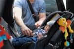 Dad fastening baby in a car seat of a small car