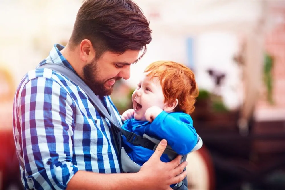 Dad wearing his laughing toddler in a front baby carrier