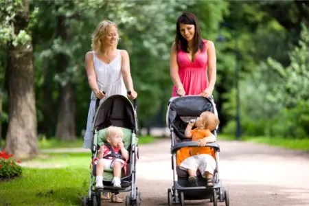 Two moms walking their babies in strollers at the park