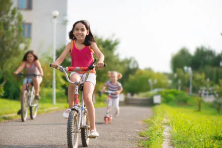 Three children riding bicycles and a scooter