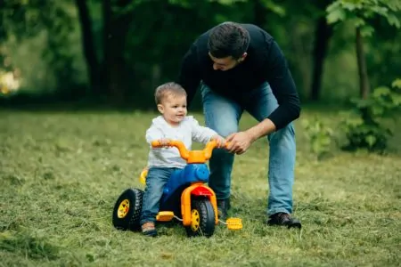 Father teaching toddler how to ride a tricycle