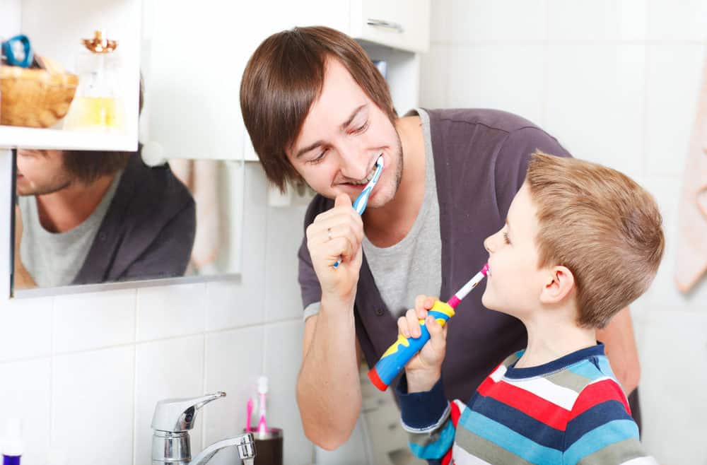 Father teaching son to use an electric toothbrush