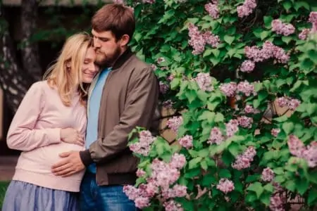 Pregnant couple standing beside a flower bush