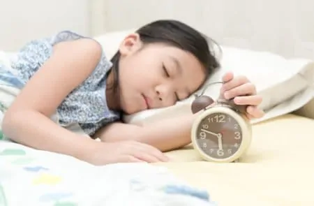 Little girl sleeping while holding an alarm clock