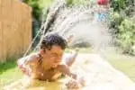 LIttle boy playing outside on a water slip and slide