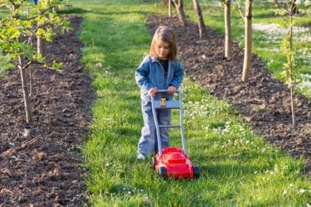 Little girl playing with a toy lawn mower outdoors