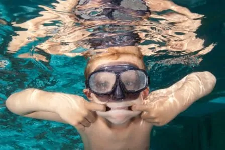 A young goofy boy swimming with goggles
