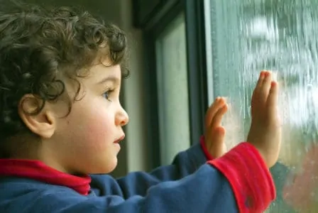 Little boy watching the rain through a window