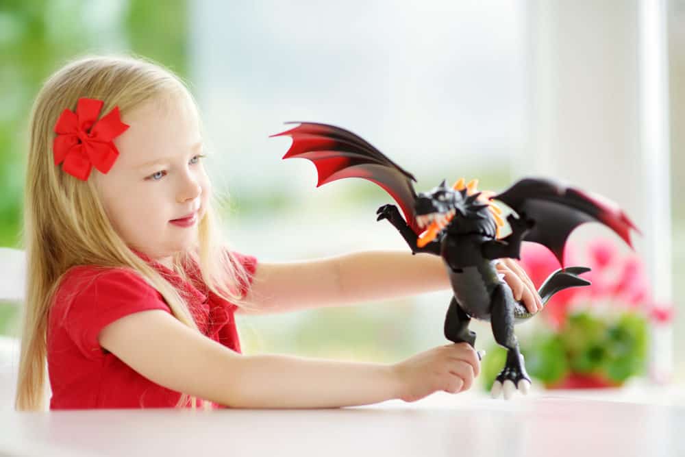 Cute little girl playing with toy dragon at home