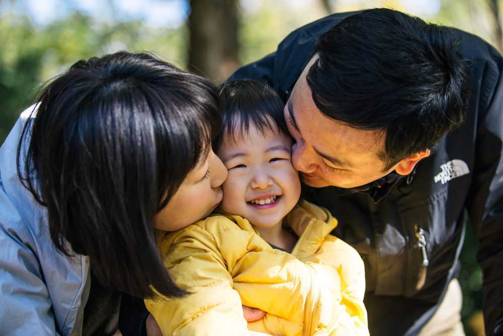 Happy japanese parents kissing their daughter on the cheeks
