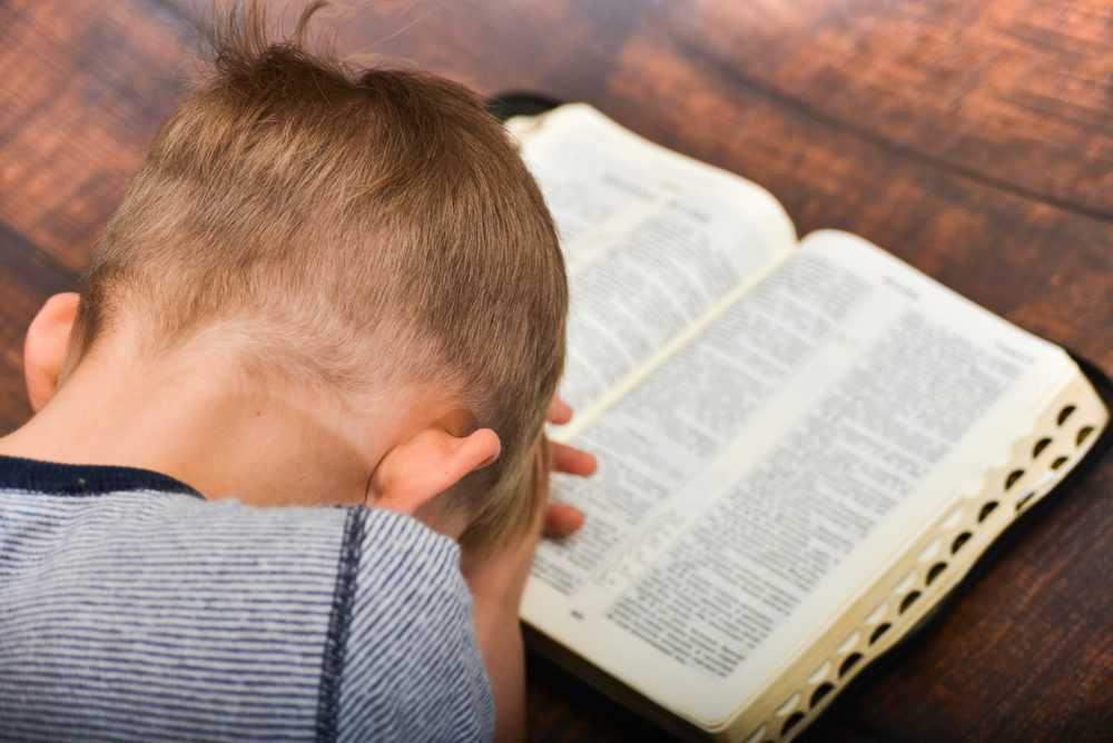 Young boy praying over an open Bible