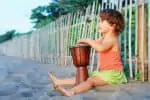 Little happy girl playing traditional african hand drum djembe
