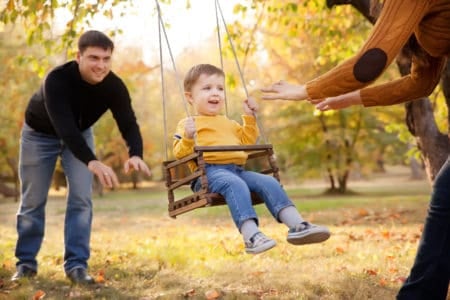 Mom and dad pushing toddler on an outdoor swing