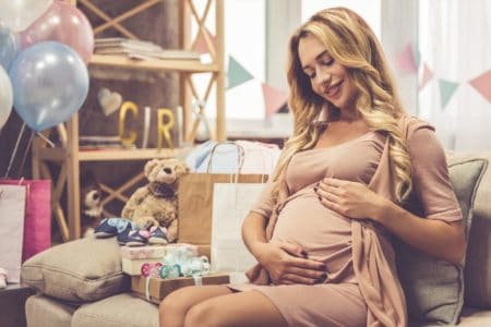 A pregnant woman in a beautiful baby shower dress is smoothing her tummy