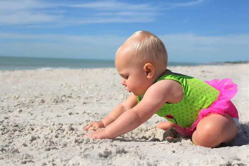A cute baby in a swimsuit playing in the sand at the beach