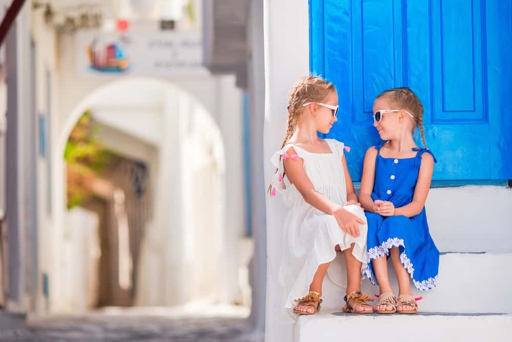 Two happy little girls looking at each other on the street of Mykonos in Greece