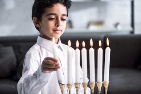 Cute Hebrew boy lighting menorah candles