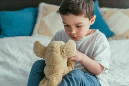 Cute toddler kid looking at soft toy in bedroom