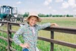 Smiling young boy wearing hat leaning on fence in the farm