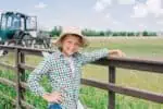 Smiling young boy wearing hat leaning on fence in the farm