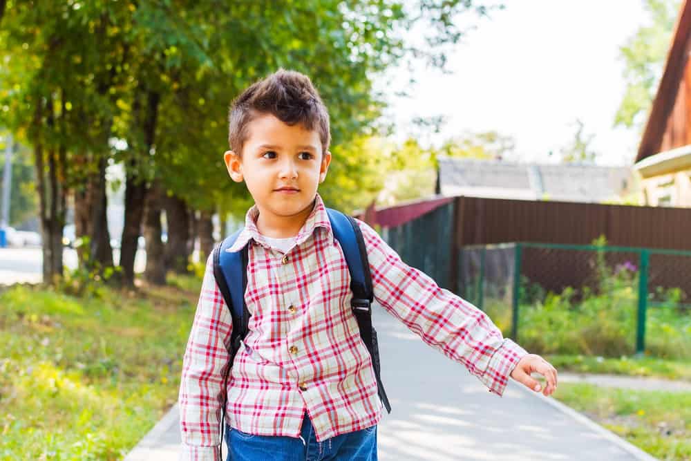 Adorable young boy with a backpack walking in the alley