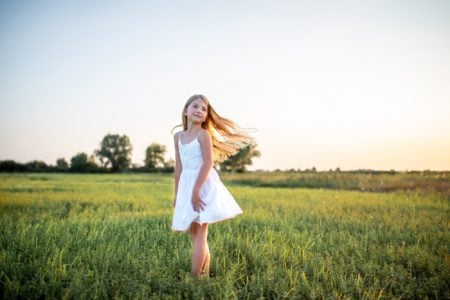 Adorable young girl wearing white dress standing in green meadow