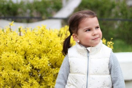 Cute little girl with ponytails wearing jacket on the background of a bush
