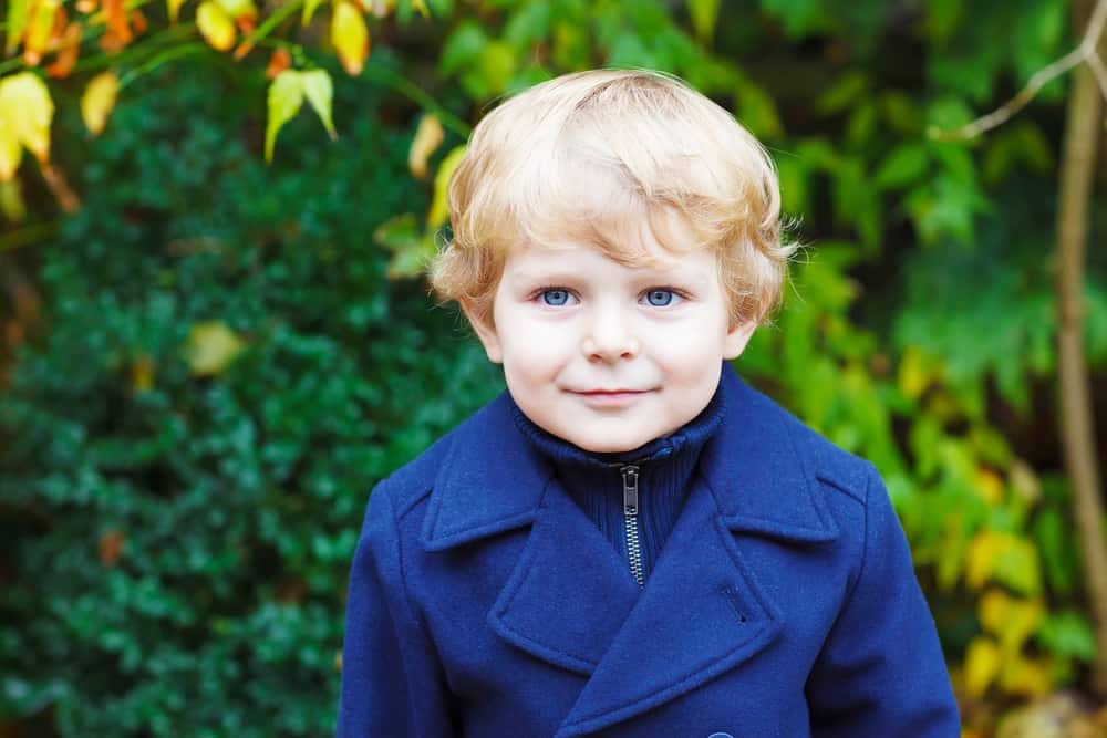 Smiling little blond boy wearing blue coat in the park