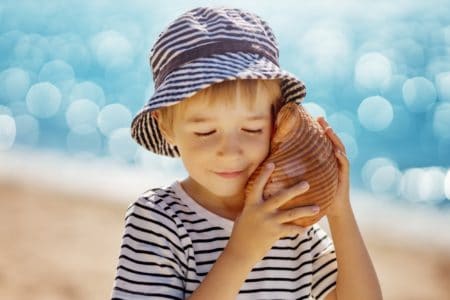 Happy little boy listening to the seashell on the beach
