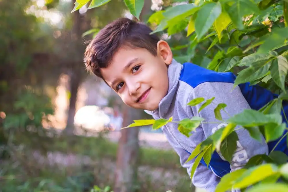 Cheerful little boy looking from behind the bushes